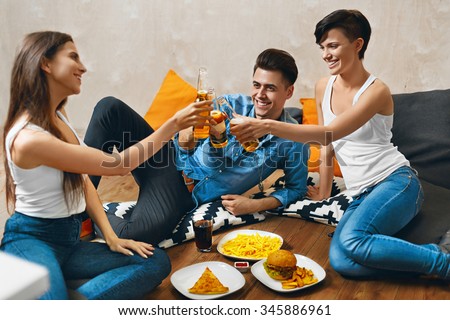 Cheers. Group Of Happy Smiling Young People Toasting Beer Bottles And Eating Fast Food. Friends Partying At Home, Sitting On The Floor. Celebration, Friendship, Leisure, People Concept