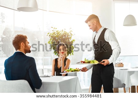 Happy Couple In Love Having Romantic Dinner In Luxury Gourmet Restaurant. Waiter Serving Meal. People Celebrating Anniversary Or Valentine\'s Day. Romance, Relationship Concept. Healthy Food Eating.