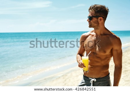 Summer Relax. Portrait Of Athletic Sexy Man With Muscular Body Drinking Fresh Juice Smoothie Cocktail On Tropical Beach. Handsome Fitness Male Model Sunbathing, Enjoying Refreshing Drink On Vacation