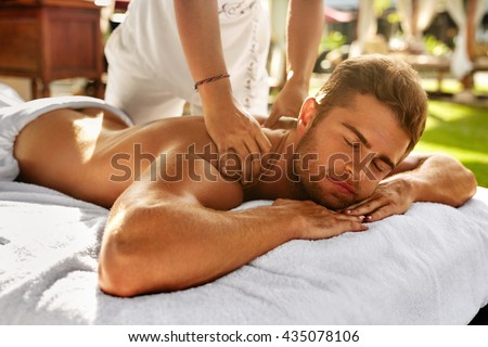Spa Massage For Man. Close Up Of Handsome Healthy Smiling Man Enjoying Relaxing Back Massage At Outdoor Beauty Salon. Masseuse Massaging Male Body With Aromatherapy Oil. Skin Care Treatment Concept
