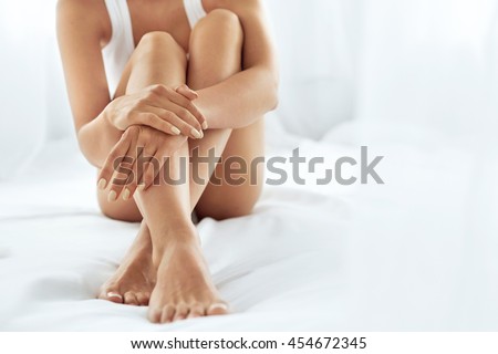 Woman Body Care. Close Up Of Long Female Legs With Perfect Smooth Soft Skin, Pedicure And Beautiful Hands With Natural Manicure, Healthy Nails On White Bed. Epilation, Beauty And Health Concepts