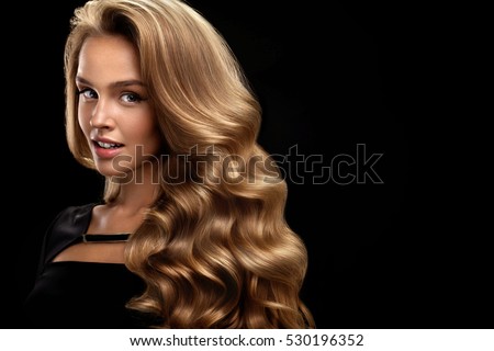 Beautiful Curly Hair. Female Beauty Model With Perfect Makeup, Gorgeous Volume And Blonde Hair Color. Attractive Smiling Woman With Healthy Long Shiny Wavy Hair On Black Background. High Resolution