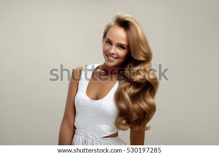Perfect Hair. Beautiful Smiling Woman Model With Long Shiny Blonde Wavy Curly Hair On White Background. Portrait Of Sexy Girl With Natural Makeup, Beauty Face And Fashion Hairstyle. High Resolution