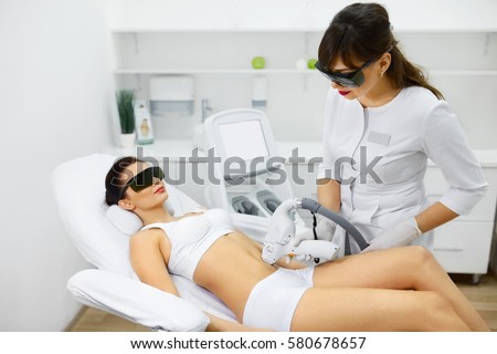 Cosmetology. Young Woman With Beautiful Body At Spa Salon Receiving Laser Hair Removal Procedure. Beautician Using Modern Apparatus For Spa Procedures. Skin And Beauty Care. High Resolution
