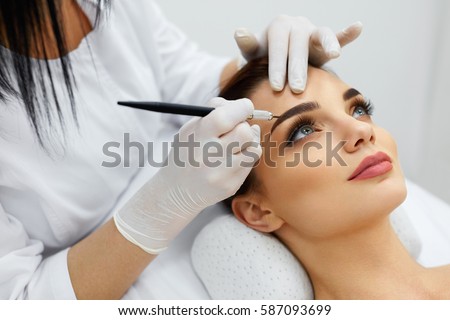 Permanent Makeup For Eyebrows. Closeup Of Beautiful Woman With Thick Brows In Beauty Salon. Beautician Doing Eyebrow Tattooing For Female Face. Beauty Procedure. High Resolution