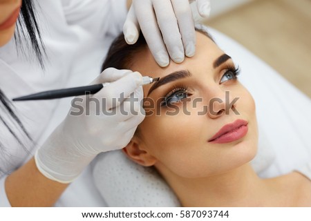 Make-Up. Beautician Hands Doing Eyebrow Tattoo On Woman Face.Permanent Brow Makeup In Beauty Salon. Closeup Of Specialist Doing Eyebrow Tattooing For Female. Cosmetology Treatment. High Resolution