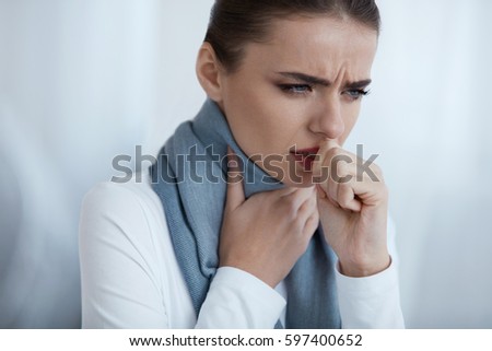 Cold And Flu. Portrait Of Beautiful Young Female With Cough And Sore Throat Feeling Sick Indoors. Closeup Of Ill Unhealthy Woman In Scarf Coughing, Caught Cold. Health Care Concept. High Resolution