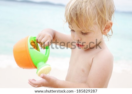 Child pouring water from a watering can onto his hand, beach or pool play time