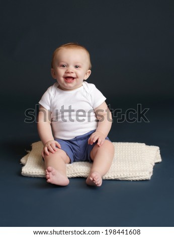 Happy baby laughing and smiling, sitting on a white blanket, dark blue studio backdrop