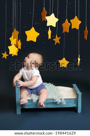 Baby sitting in bed, looking up, against a dark blue background. Nap time, sleeping concept