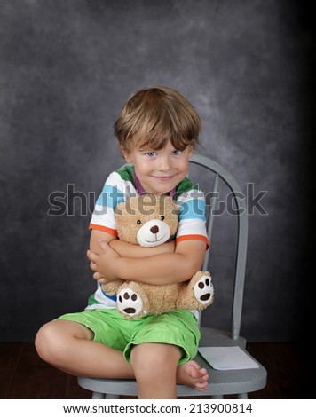 Child on chair in classroom hugging a stuffed bear toy, \