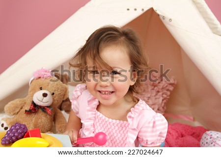 Happy toddler girl engaged in pretend play tea party indoors at home with a teepee tent