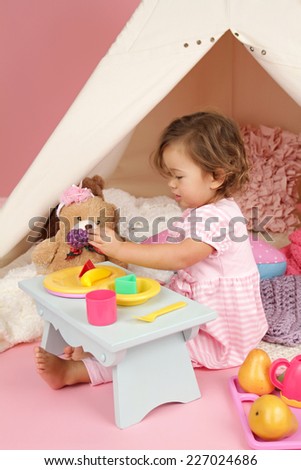 Happy toddler girl engaged in pretend play tea party indoors at home with a teepee tent