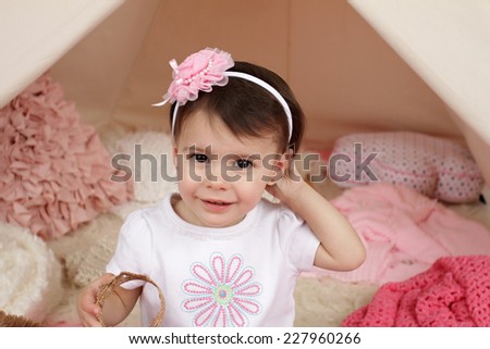 Toddler child, kid, engaged in pretend play with a pink flower headband and teepee tent