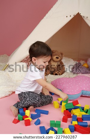 Toddler child, kid, engaged in pretend play with building blocks, toys, and teepee tent