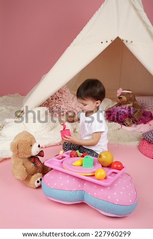 Toddler child, kid, engaged in pretend play with food, stuffed toys, and teepee tent