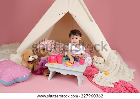 Toddler child, kid, engaged in pretend play with food, stuffed toys, and teepee tent