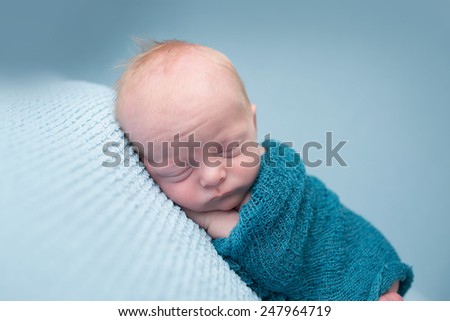 Newborn infant baby asleep posed on a blanket, in a knit wrap
