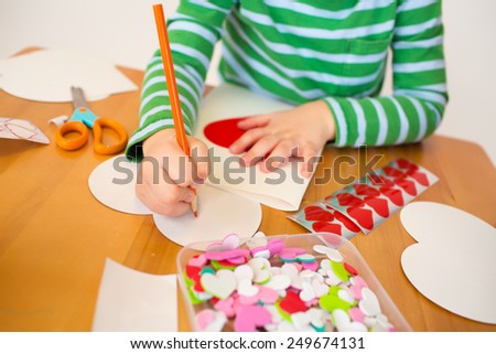 Child doing Valentine\'s day arts and crafts with hearts, pencils, paper
