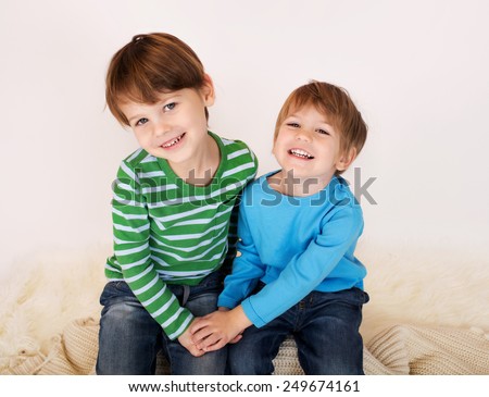 Two kids (children, brothers, siblings), laughing, hugging and looking at the camera holding hands