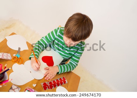Child doing Valentine\'s day arts and crafts with hearts, pencils, paper