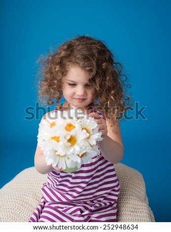 Happy smiling child looking at camera: girl with curly hair holding flowers, Easter or spring theme