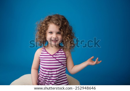 Happy smiling laughing child looking at camera: girl with curly hair holding something or pointing at something