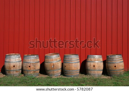 Wine barrels at a vineyard against a red barn wall, rural scene