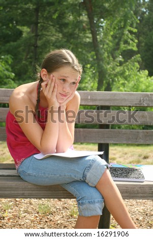 School girl thinking and working on difficult homework assignment in a park on a bench