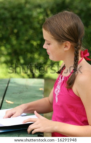 School girl writing in notebook, planner in an outdoors setting