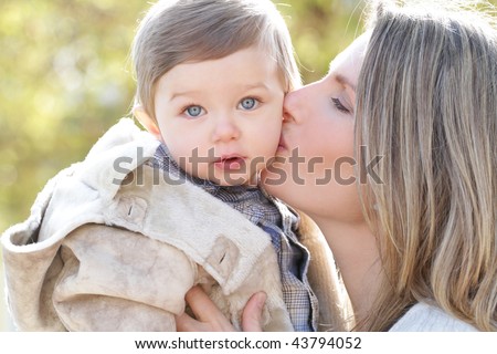 Family: mother kissing her baby son outdoors, fall, seasonal theme