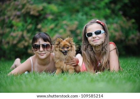 Two girl friends in sunglasses laying on a lawn with a puppy