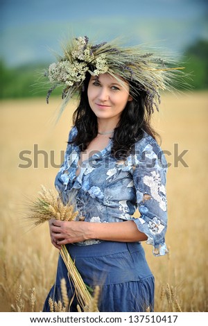 Woman with a flower crown in the wheat field holding a bunch of wheat