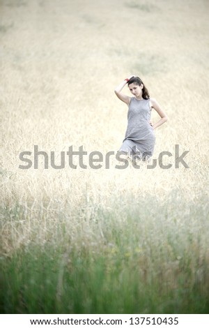 Wide shot of a young woman in a grey linen dress posing in the field