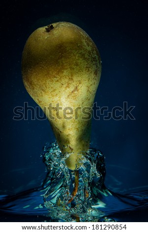 A studio shot of a pear coming out of the water surface against blue background