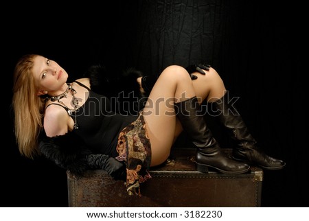 Blond girl in fancy clothes laying on old leather trunk