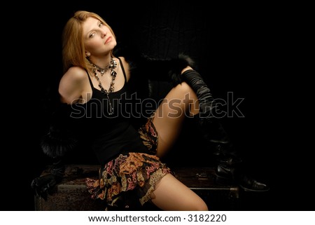 Blond girl in fancy clothes sitting on old leather trunk