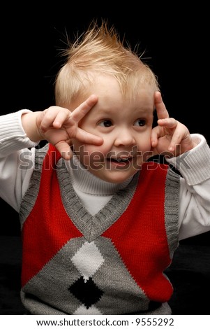Close-up of a boy in red vest looking sideways making faces playing with his hands