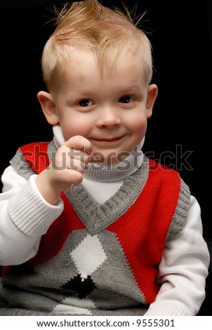 Boy in red vest smiling holding hand to his face looking sideways