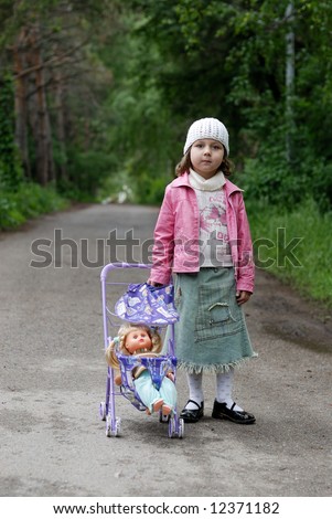 Little girl with toy stroller and doll against green alley