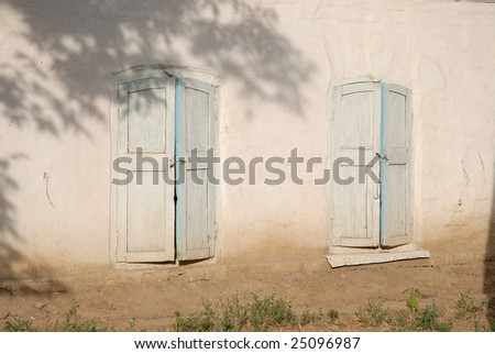 Old light blue wooden shuttered windows on light pink clay wall lit by the setting sun