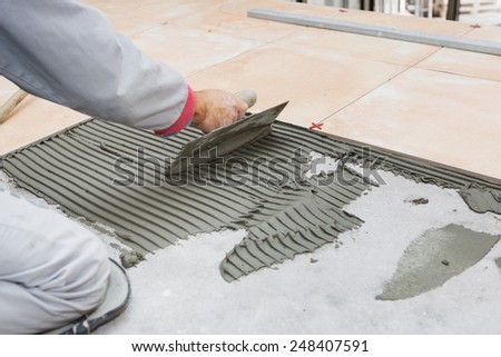 Home improvement, renovation - handyman laying tile, trowel with mortar