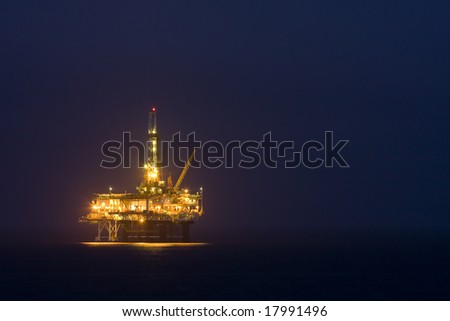 Photo of an offshore drilling rig off the coast of a city in the the US at night - landscape.