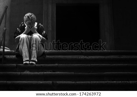Poor and afflicted woman with hands on face sitting on the steps of a church