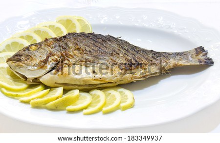 Grilled sea bream with lemon slices on white plat