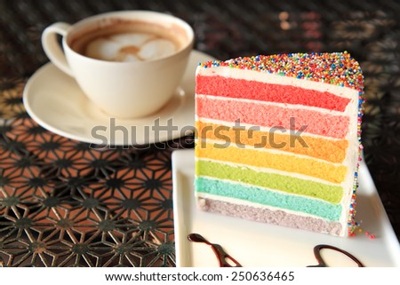 A cup of coffee and Slice of colourful rainbow layered birthday cake