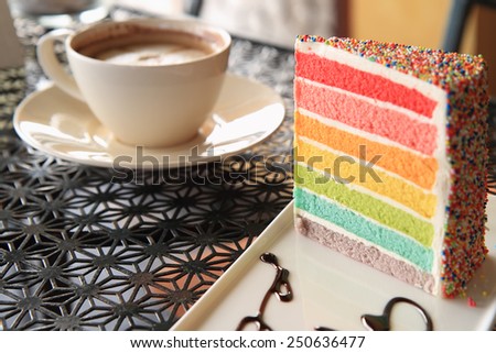 A cup of coffee and Slice of colourful rainbow layered birthday cake
