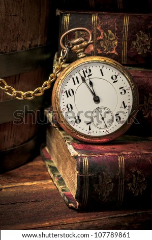 Antique pocket clock showing a few minutes to midnight over ancient books in Low-key. Concept of time,the past or deadline.