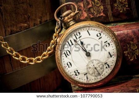 Antique pocket clock showing a few minutes to midnight over ancient books in Low-key. Concept of time,the past or deadline.