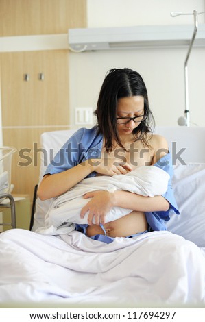 Beautiful new mother happy holding her infant baby feeding her milk after giving birth in hospital.